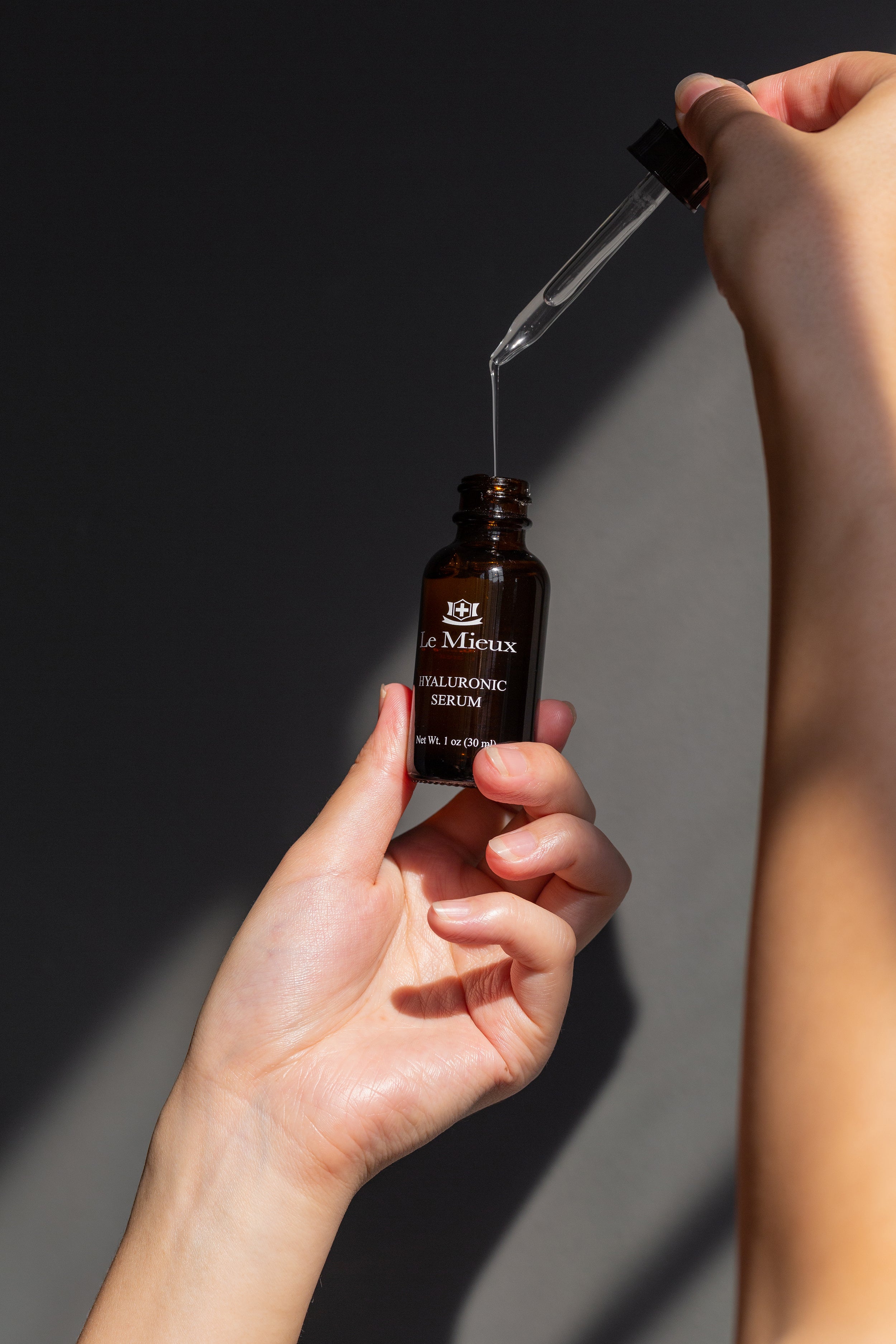 Hyaluronic Serum and dropper being held up against dark grey background.