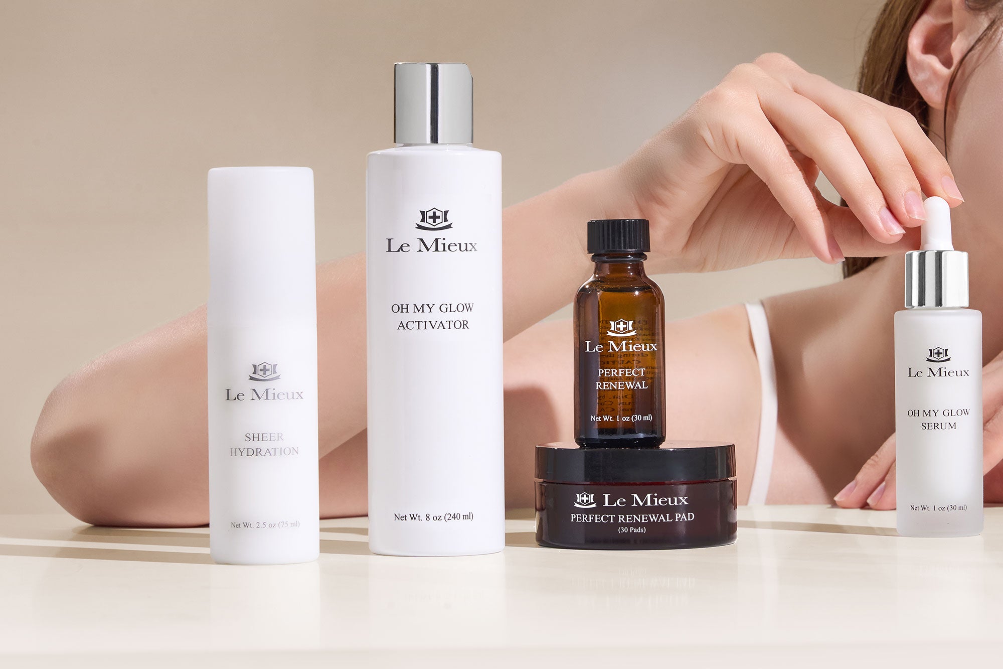 Collection of Le Mieux skincare products on a neutral background with a person holding a serum dropper