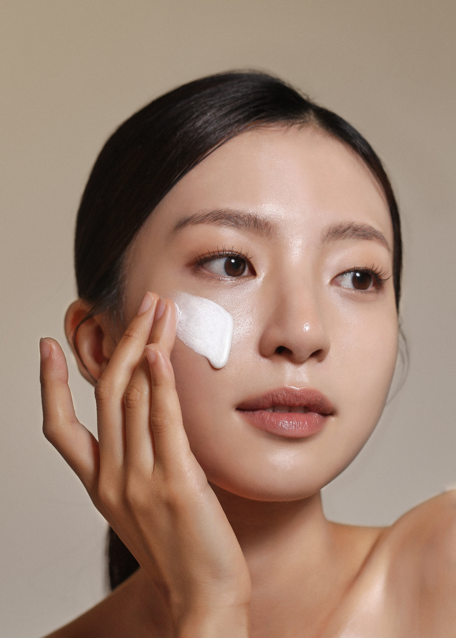 Woman applying Peptide Foam Cleanser to face against a neutral background