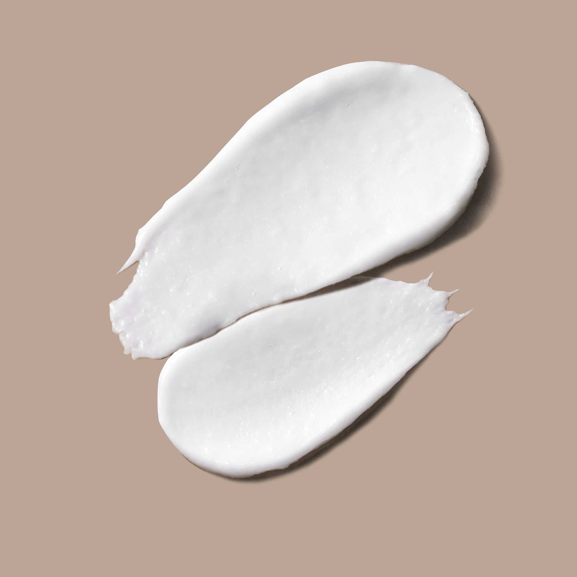 Two white swatches of Microderm Exfoliant on a light brown background.