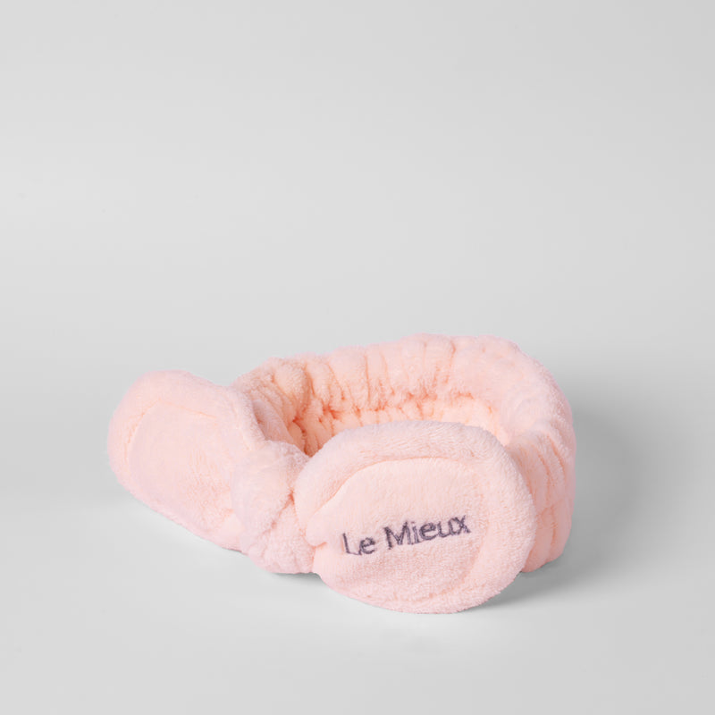 Pink headband with the "Le Mieux" logo on one side of the bow isolated in front of a light gray background.