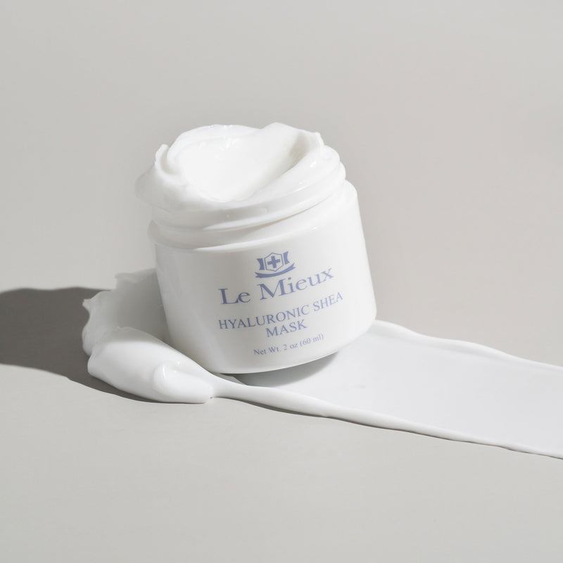 White opened container of Hyaluronic Shea Mask on a large swatch of creamy white mask texture in front of light grey background.