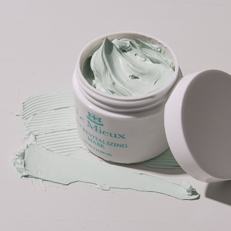 Open white container that reads "Icy Revitalizing Mask" with Le Mieux logo on it resting on top of swabs of light green mask texture. Container lid is resting against the right side of the container. All on light grey background.