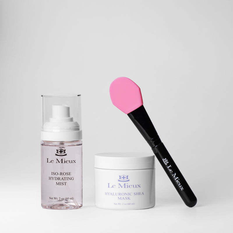 2 oz Iso-Rose Hydrating Mist next to a white Hyaluronic Shea Mask container with a black and pink applicator leaning against it. All isolated on a light gray background.