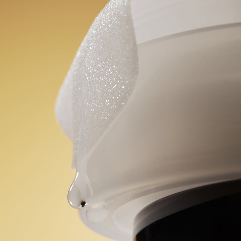 Soaked single Vita-C Pad hanging over the side of a white container in front of a yellow background.